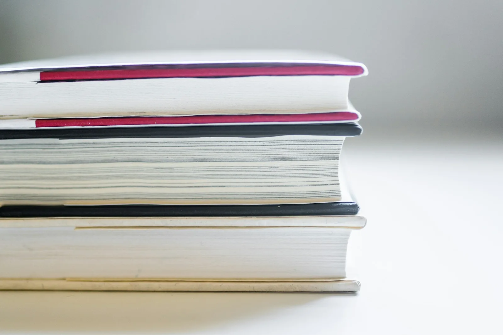 The page edges of three hardcover books stacked on a light surface.
