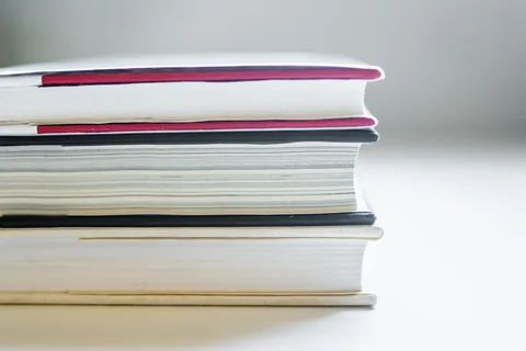 The page edges of three hardcover books stacked on a light surface.