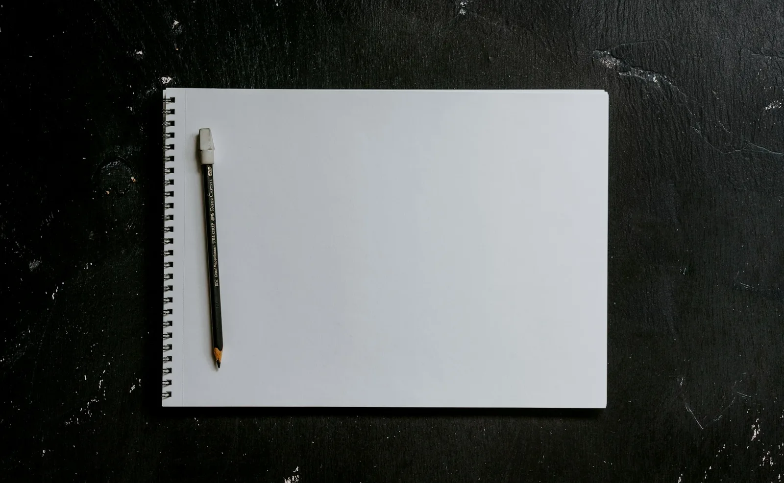 A pencil resting on a blank spiral notebook on a dark wooden surface.