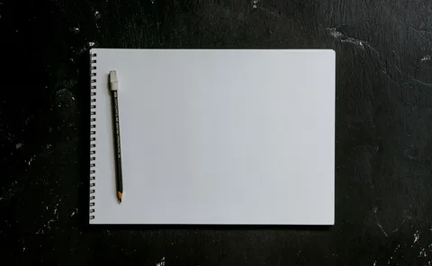 A pencil resting on a blank spiral notebook on a dark wooden surface.