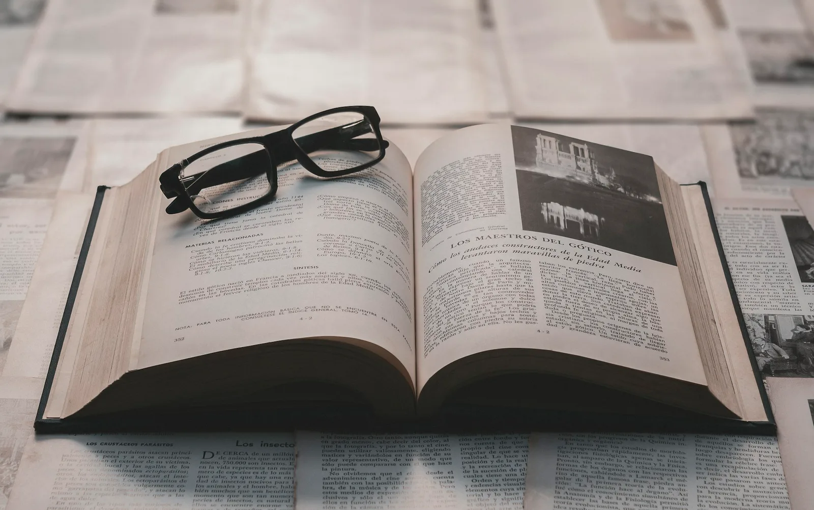 Reading glasses resting on an open book surrounded by printed pages.