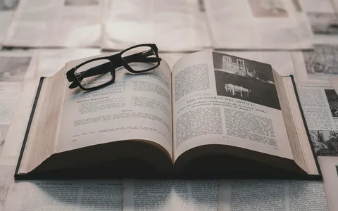 Reading glasses resting on an open book surrounded by printed pages.